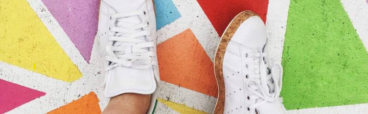 Feet in white sneakers on colorfully painted pavement.